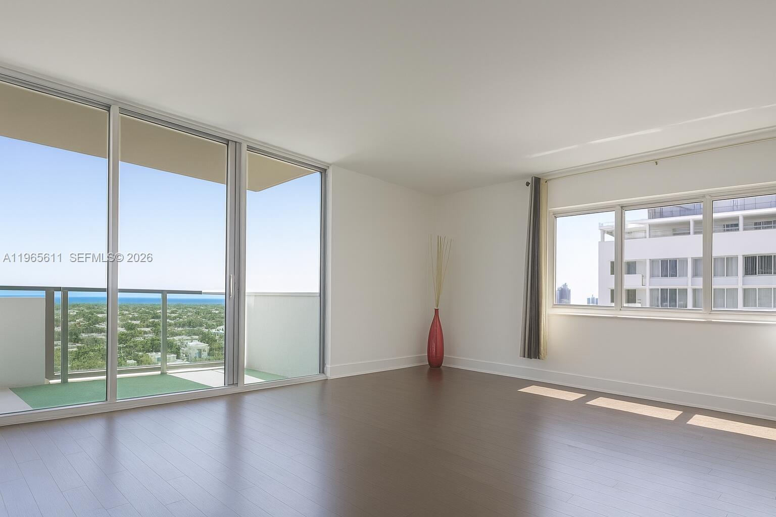 An empty room features dark wood flooring, white walls, large windows, and a balcony — 1200 West Ave # 1507, Miami Beach FL 33139, MIAMI BEACH, FL
