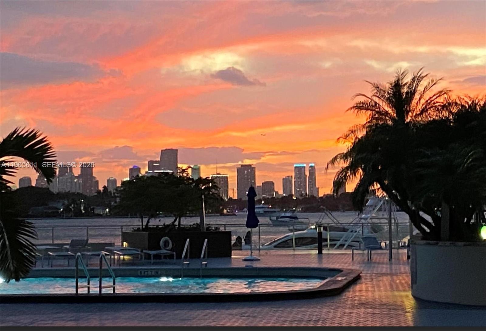 A swimming pool overlooks a waterfront view of a city skyline at sunset — 1200 West Ave # 1507, Miami Beach FL 33139, MIAMI BEACH, FL