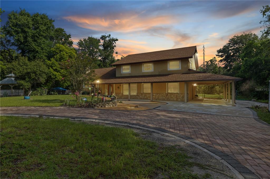 A two-story house with a stone facade, a covered porch, and a brick driveway at dusk — 230 E PANAMA ROAD, WINTER SPRINGS, FL