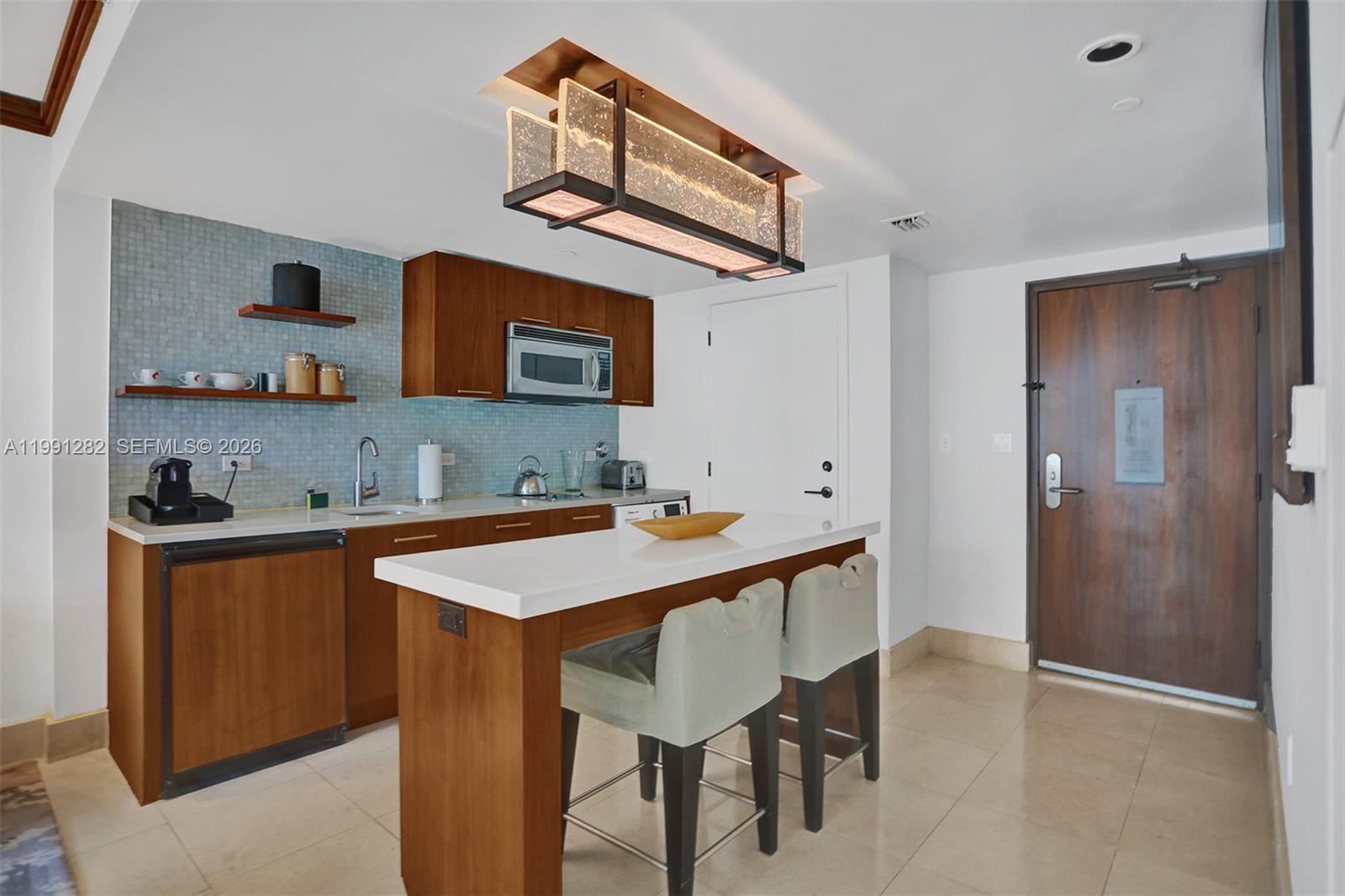 A kitchen features wood cabinets, a white island with two stools, and a light fixture — 6801 Collins Ave # 314, Miami Beach FL 33141, MIAMI BEACH, FL