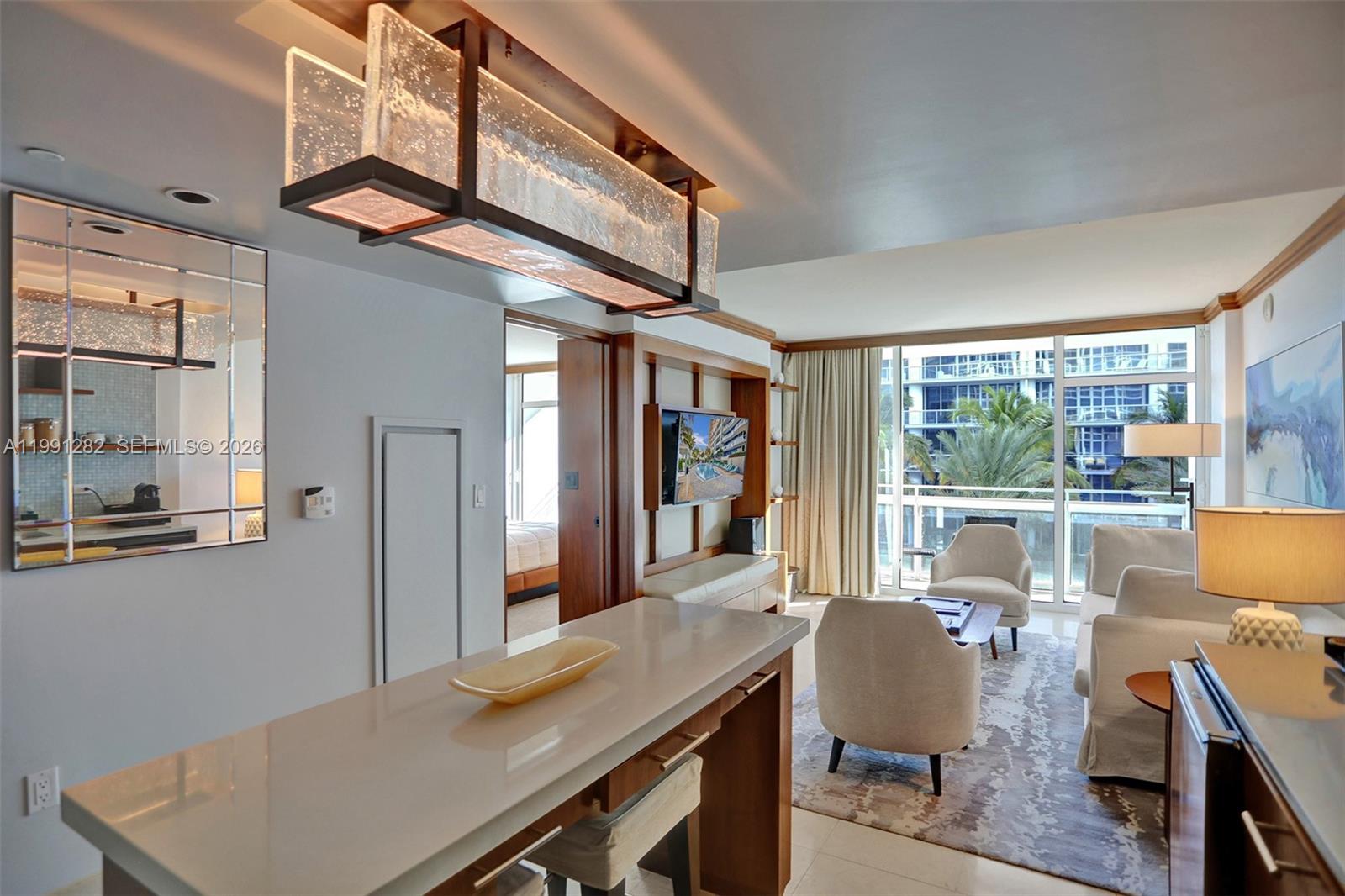 A modern living room and kitchen area with a breakfast bar, chandelier, and balcony view — 6801 Collins Ave # 314, Miami Beach FL 33141, MIAMI BEACH, FL