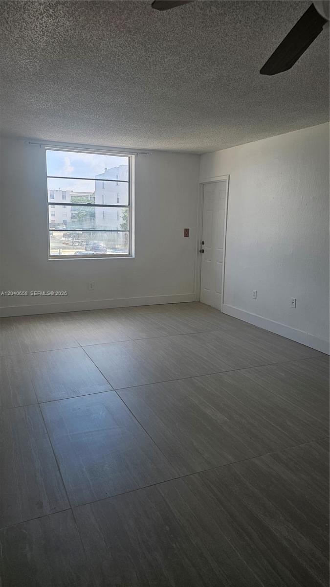 An empty room features light-colored tile flooring, white walls, a window, and a closed door — 5625 W 20th Ave # 208, Hialeah FL 33012, HIALEAH, FL