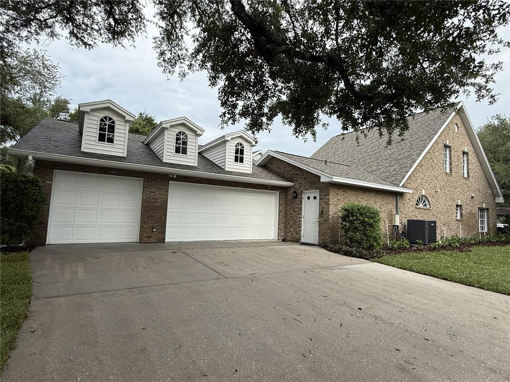 A brick house exterior features a three-car garage, three dormer windows, and a concrete driveway — 4002 W DALE AVENUE, TAMPA, FL