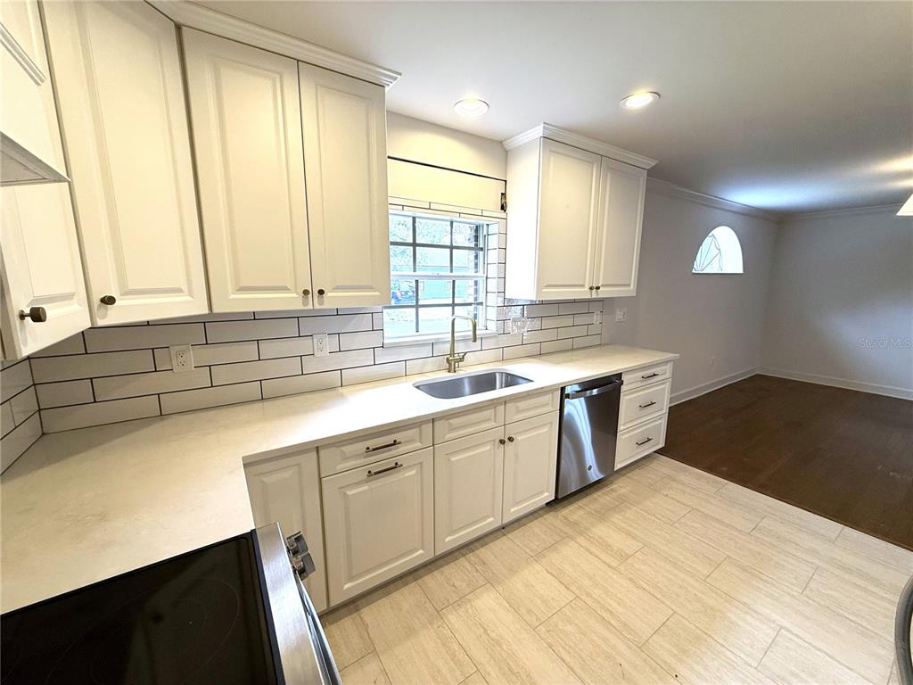 A kitchen features white cabinets, a subway tile backsplash, stainless steel appliances, and light flooring — 4002 W DALE AVENUE, TAMPA, FL