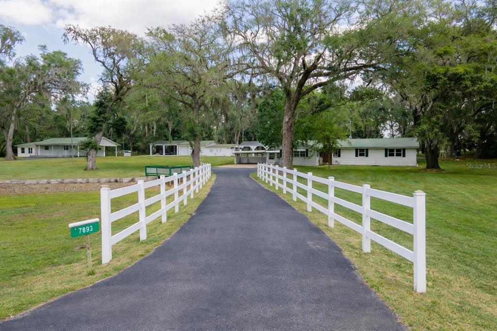 A paved driveway leads toward a white house framed by a white fence and trees — 7893 S US HIGHWAY 441, LAKE CITY, FL