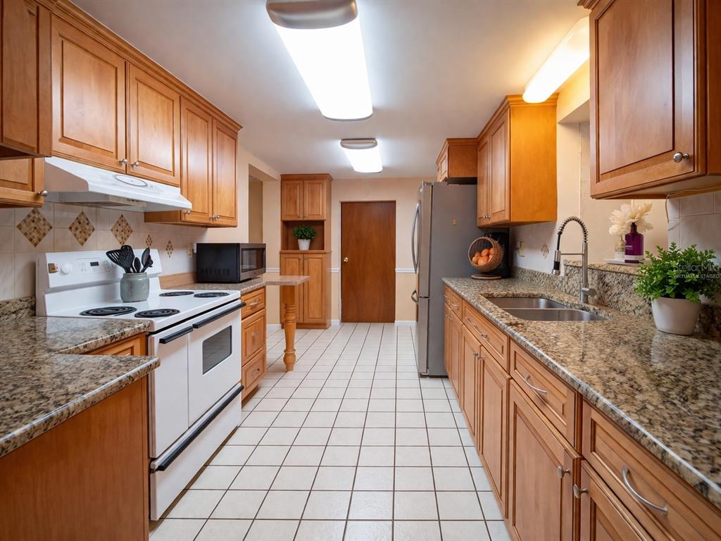 A kitchen with light wood cabinets, granite countertops, white appliances, and white tiled flooring — 7893 S US HIGHWAY 441, LAKE CITY, FL