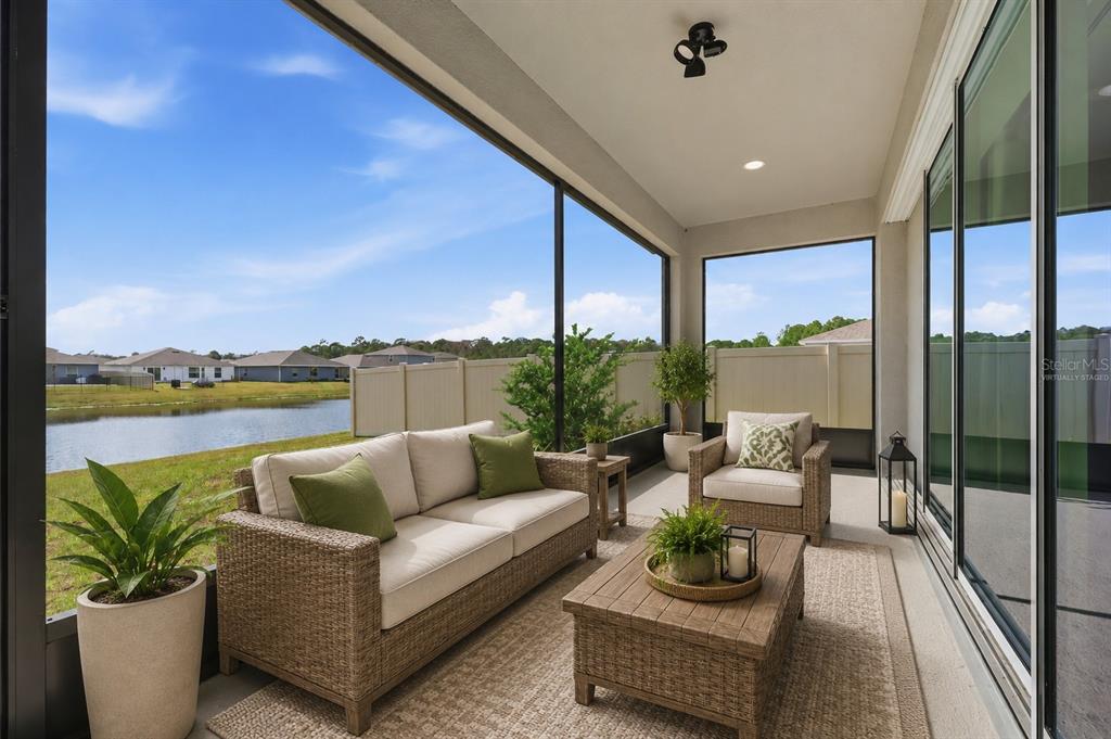 A screened-in patio features wicker furniture, a rug, and a view of a pond — 4698 CORAL HARBOUR ROAD, KISSIMMEE, FL