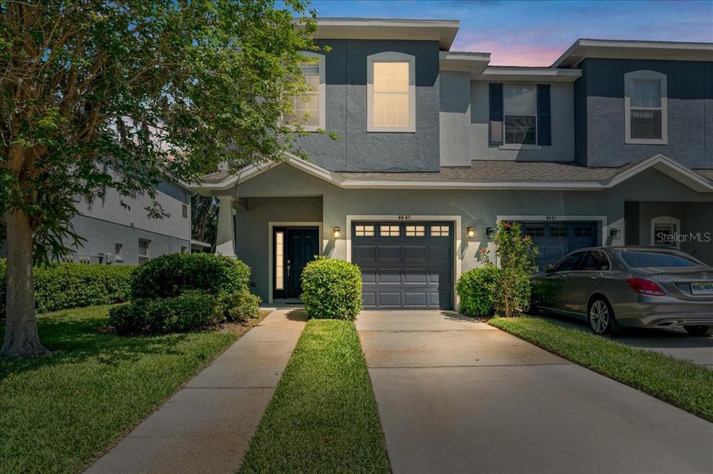 A two-story townhouse exterior with a gray garage, a concrete driveway, and a small lawn — 4445 AMBERLY OAKS COURT, TAMPA, FL