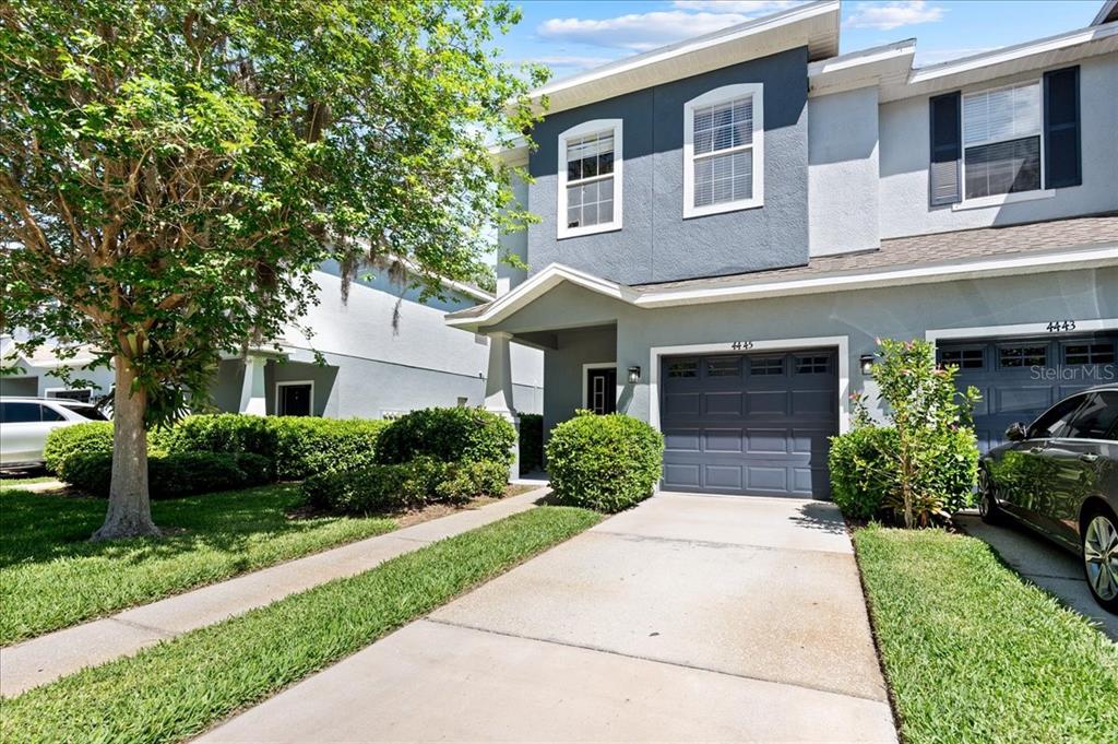 A two-story townhouse with a gray garage, stucco exterior, and a concrete driveway — 4445 AMBERLY OAKS COURT, TAMPA, FL