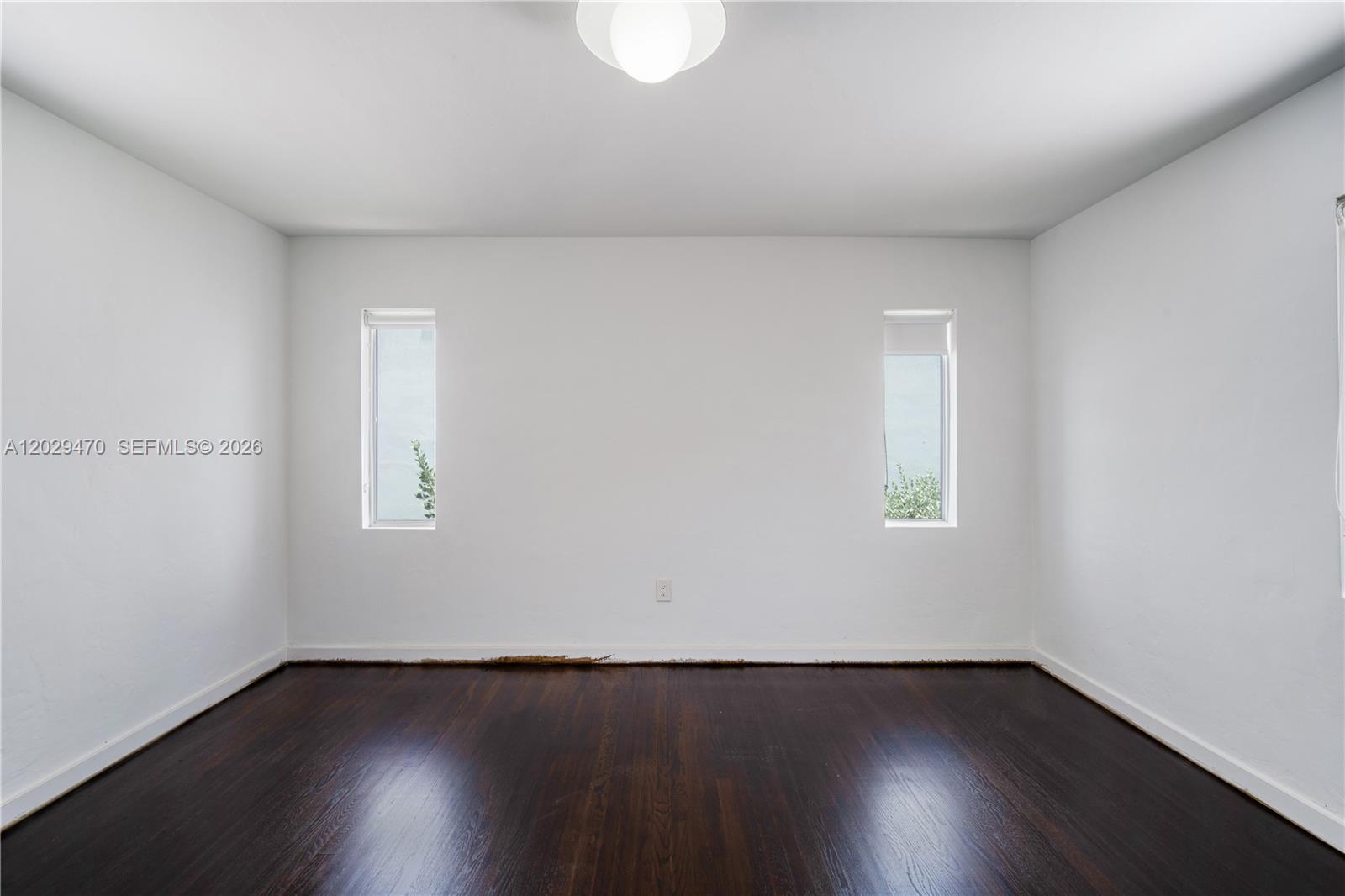 An empty room features white walls, dark hardwood floors, and two narrow vertical windows — 550 W 49th St, Miami Beach FL 33140, MIAMI BEACH, FL