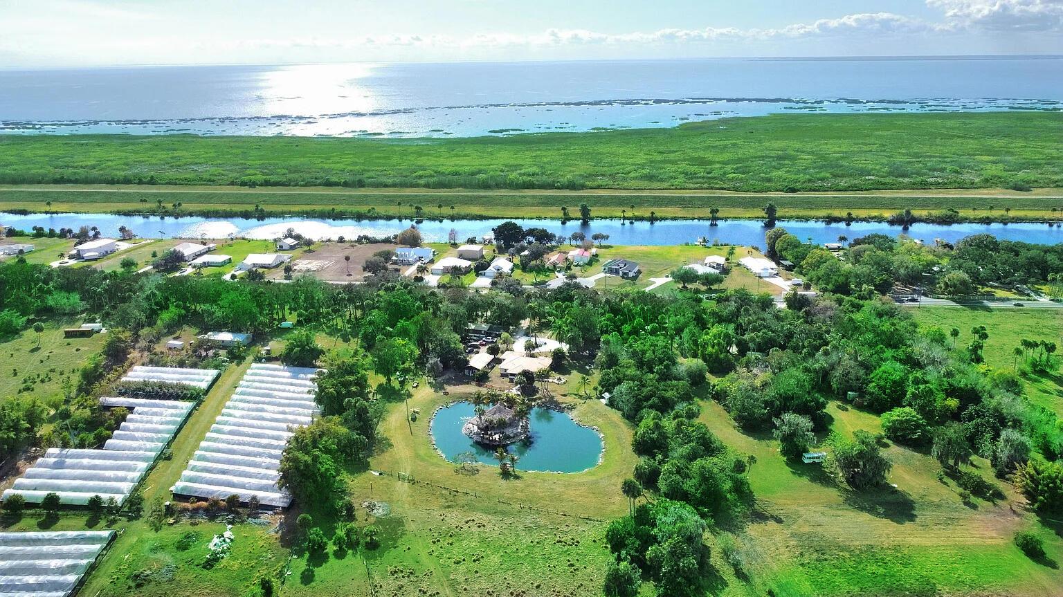 Aerial view of a property featuring a pond, greenhouse structures, and a nearby canal — 12963 Us Hwy 441 SE, Okeechobee FL 34974, OKEECHOBEE, FL
