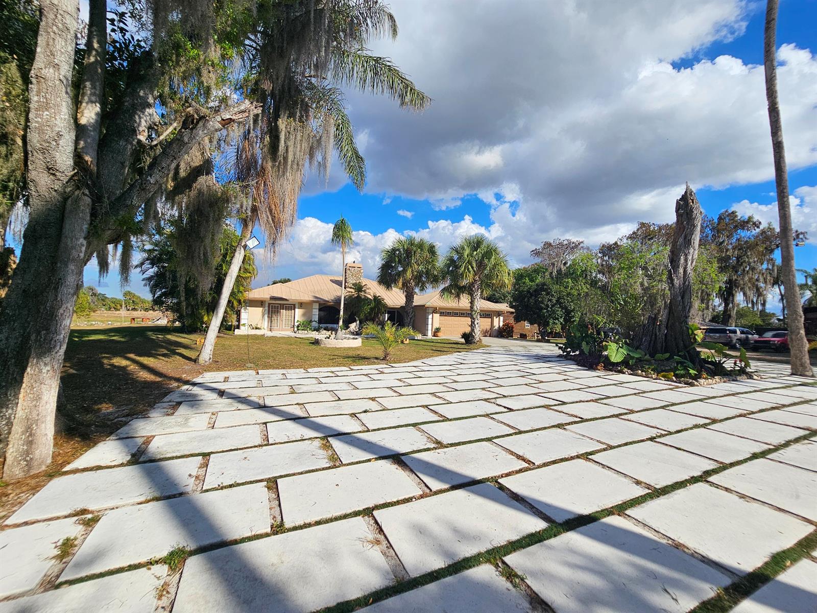 A large concrete paver driveway leads to a single-story house with palm trees and landscaping — 12963 Us Hwy 441 SE, Okeechobee FL 34974, OKEECHOBEE, FL