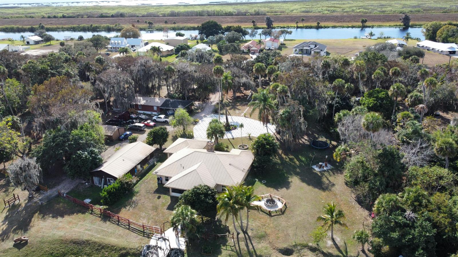 An aerial view shows a house with a metal roof, surrounding trees, and a fire pit — 12963 Us Hwy 441 SE, Okeechobee FL 34974, OKEECHOBEE, FL