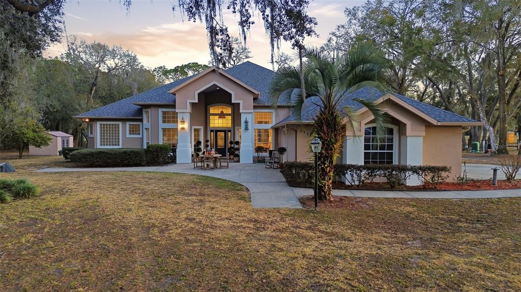 A single-story house with a tan stucco exterior, dark roof, and a front patio area — 6197 LAKE WINONA ROAD, DE LEON SPRINGS, FL