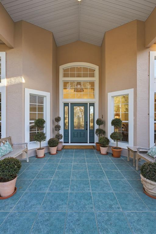 A covered entryway features blue tiled flooring, a teal front door, and potted topiary plants — 6197 LAKE WINONA ROAD, DE LEON SPRINGS, FL