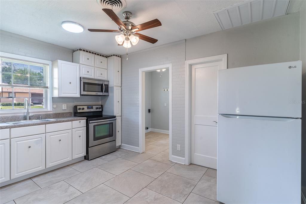 A kitchen with white cabinets, stainless steel appliances, gray brick walls, and tile flooring — 916 COHASSETT AVENUE, LAKE WALES, FL