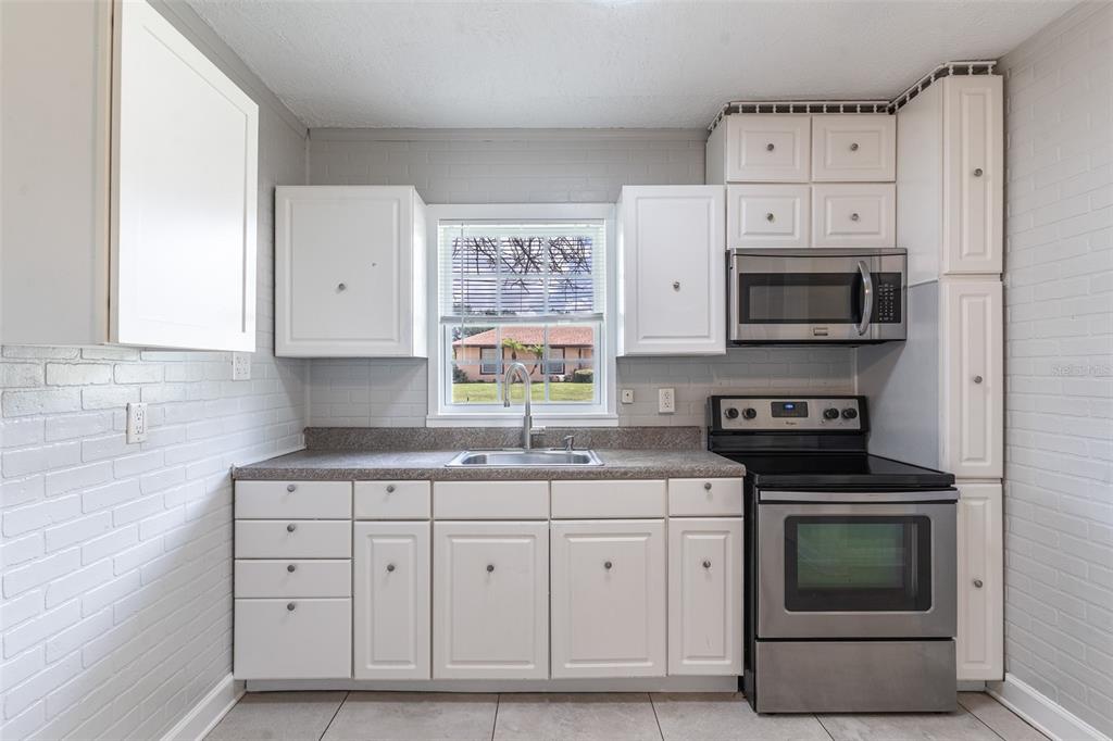 A kitchen with white cabinets, stainless steel appliances, a window, and gray brick walls — 916 COHASSETT AVENUE, LAKE WALES, FL