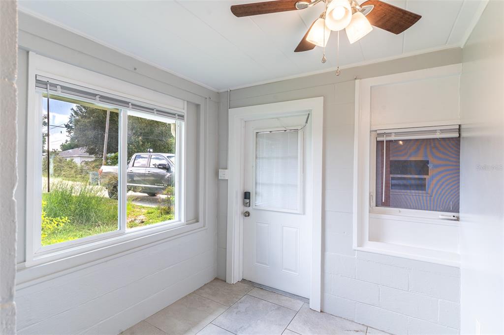A sunroom with gray block walls, tile flooring, a ceiling fan, and a white door — 916 COHASSETT AVENUE, LAKE WALES, FL