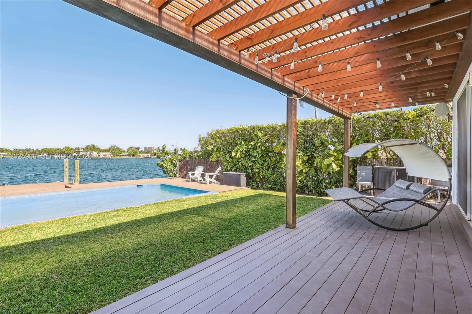 A wooden pergola covers a deck with a lounge chair overlooking a pool and water — 1231 Stillwater Dr, Miami Beach FL 33141, MIAMI BEACH, FL