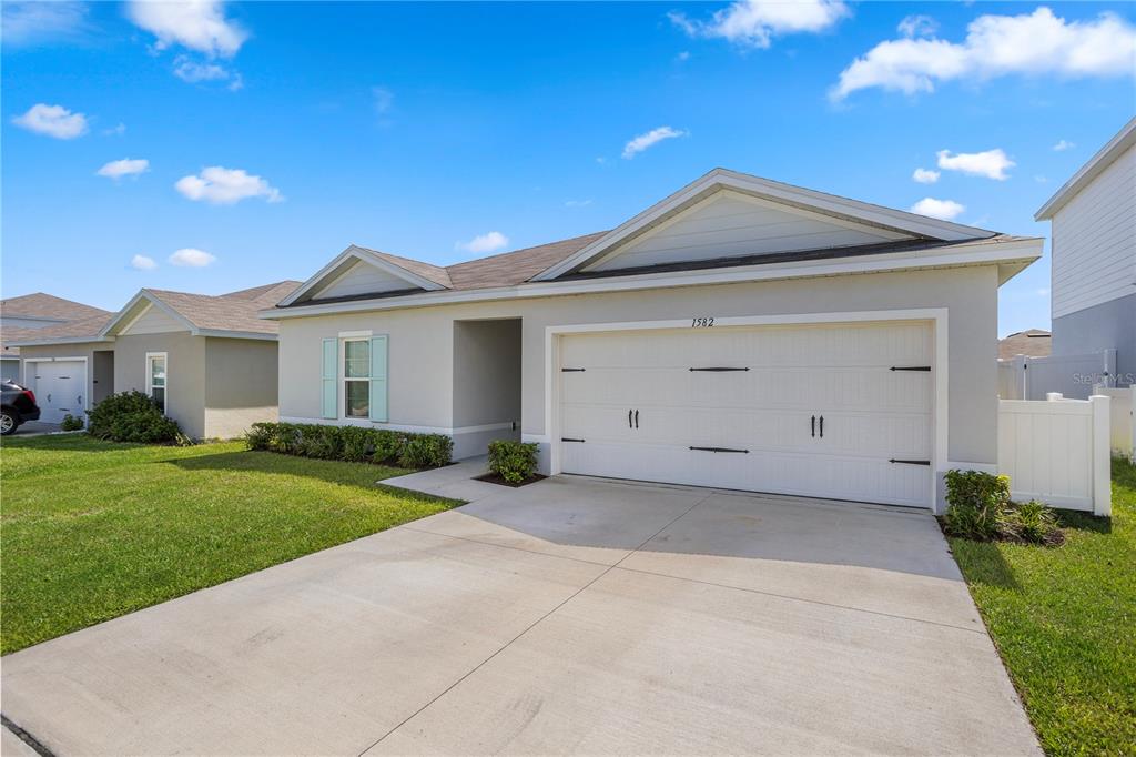 A single-story house with a white garage, light-colored siding, and a concrete driveway — 1582 FINNIGAN CIRCLE, HAINES CITY, FL
