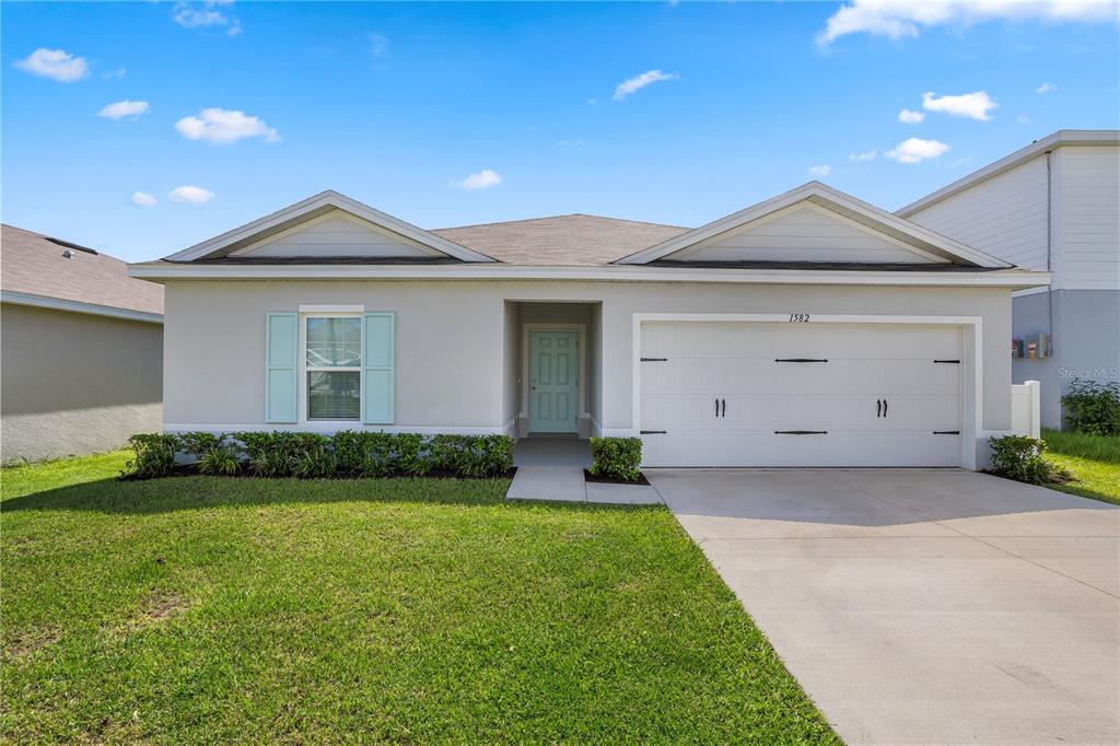 A single-story house with a light-colored exterior, a two-car garage, and a light blue front door — 1582 FINNIGAN CIRCLE, HAINES CITY, FL
