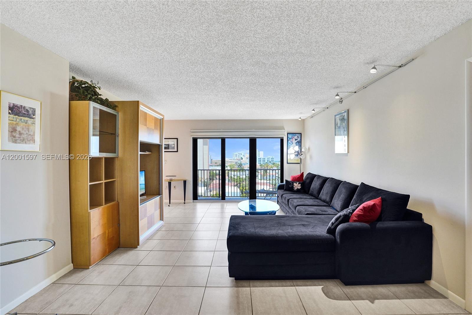 A living room features tile flooring, a large black sectional sofa, and a balcony view — 1201 S Ocean Dr # 604N, Hollywood FL 33019, HOLLYWOOD, FL