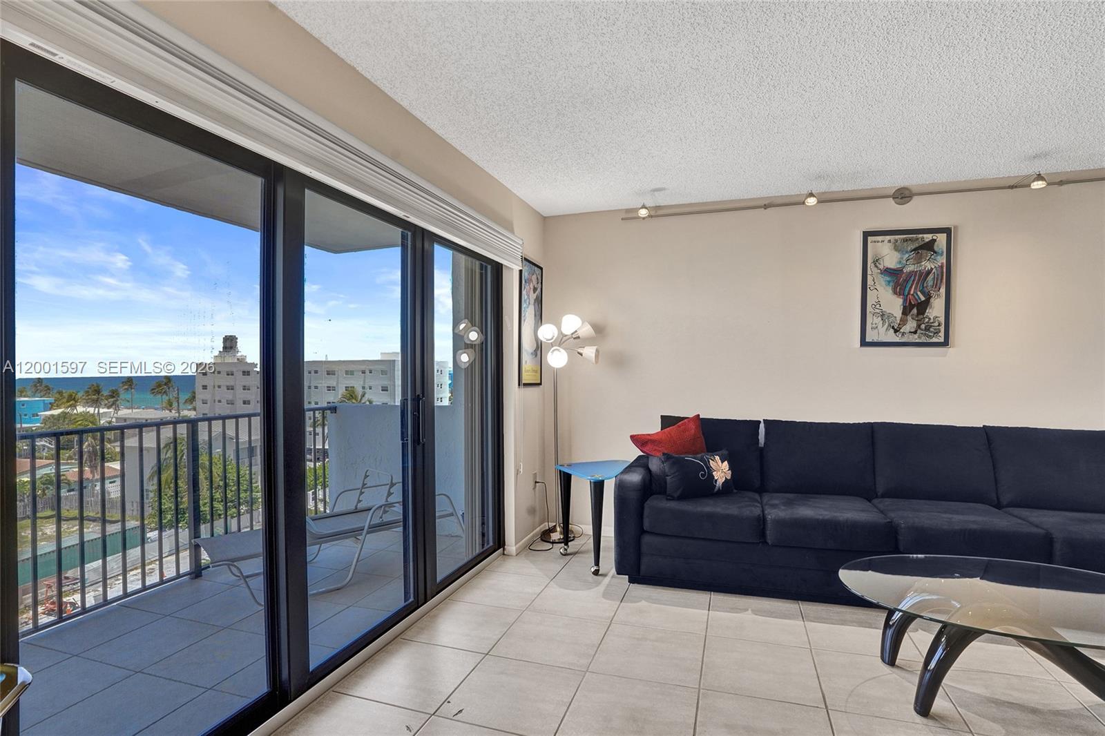 A living room features a dark sofa, tile flooring, and a balcony with ocean views — 1201 S Ocean Dr # 604N, Hollywood FL 33019, HOLLYWOOD, FL