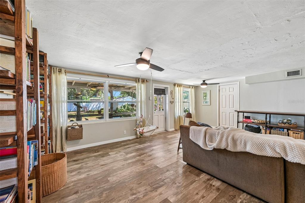 A living room features wood-look flooring, a ceiling fan, a bookshelf, and a hanging chair — 2818 11TH AVENUE W, BRADENTON, FL
