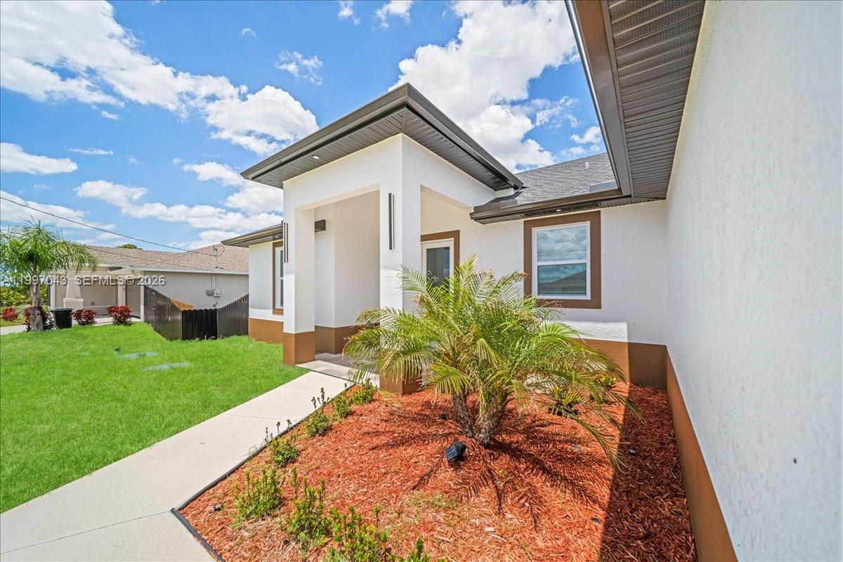 A white stucco house exterior features a covered entryway, a palm tree, and mulch landscaping — 2914 23rd st sw, Lehigh Acres FL 33976, LEHIGH ACRES, FL