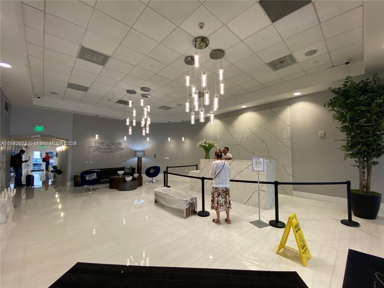 A modern lobby features a marble reception desk, pendant lighting, and a woman standing in line — 1200 Brickell Bay Dr # 3119, Miami FL 33131, MIAMI, FL