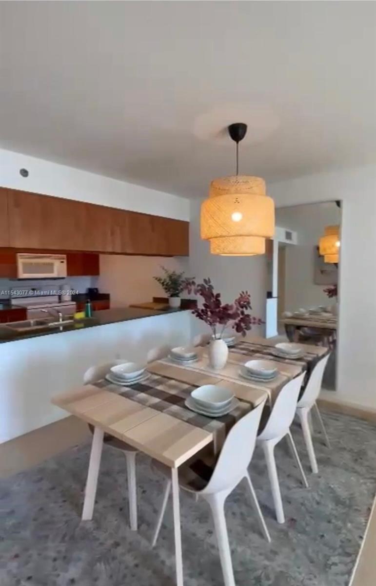 A dining area with a wooden table, white chairs, and a woven pendant light fixture — 1200 Brickell Bay Dr # 3119, Miami FL 33131, MIAMI, FL
