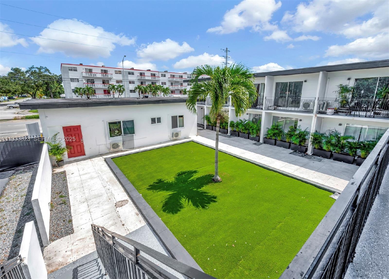 An outdoor courtyard features a central palm tree, artificial grass, and surrounding apartment building units — 14280 NE 6th Ave, North Miami FL 33161, NORTH MIAMI, FL