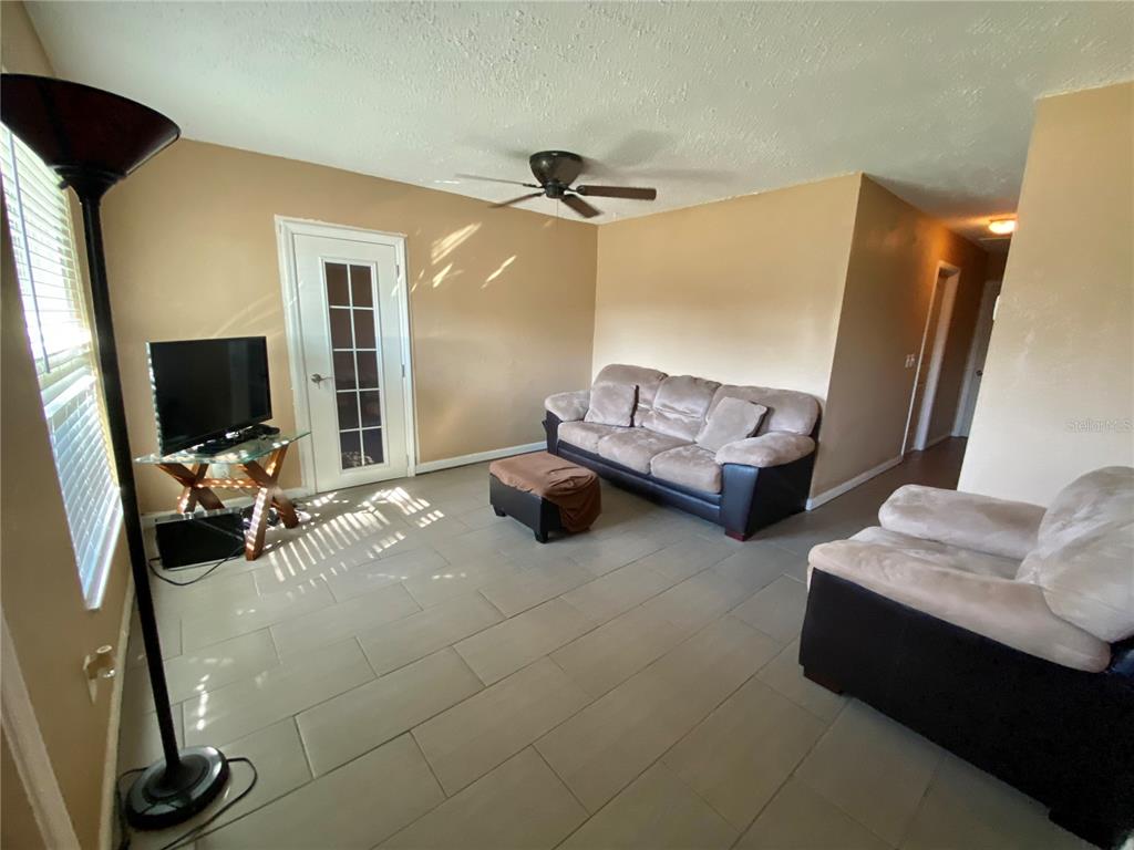 A living room features light-colored walls, tile flooring, a sofa, an ottoman, and a glass-topped table — 4403 GANDY CIRCLE, TAMPA, FL