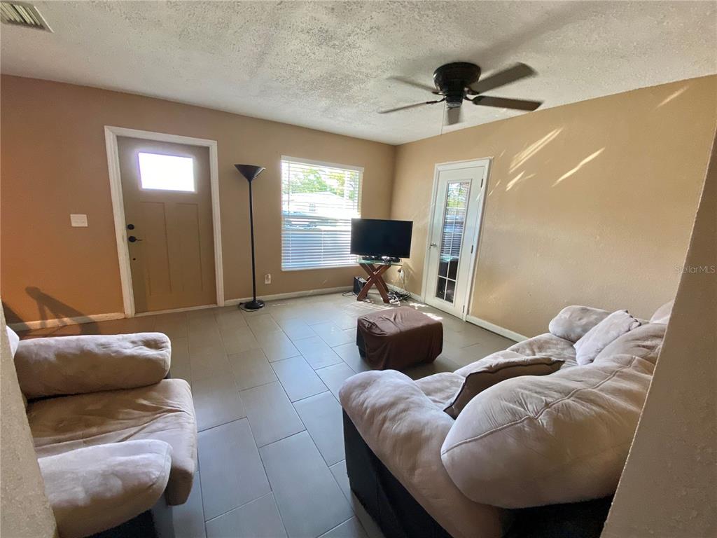 A living room features tile flooring, a ceiling fan, a television, and two sofas — 4403 GANDY CIRCLE, TAMPA, FL