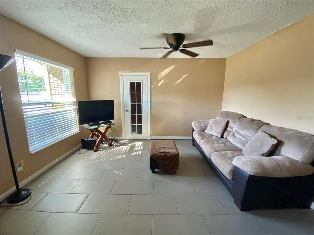 A living room features light-colored tile flooring, a beige sofa, a ceiling fan, and a door — 4403 GANDY CIRCLE, TAMPA, FL