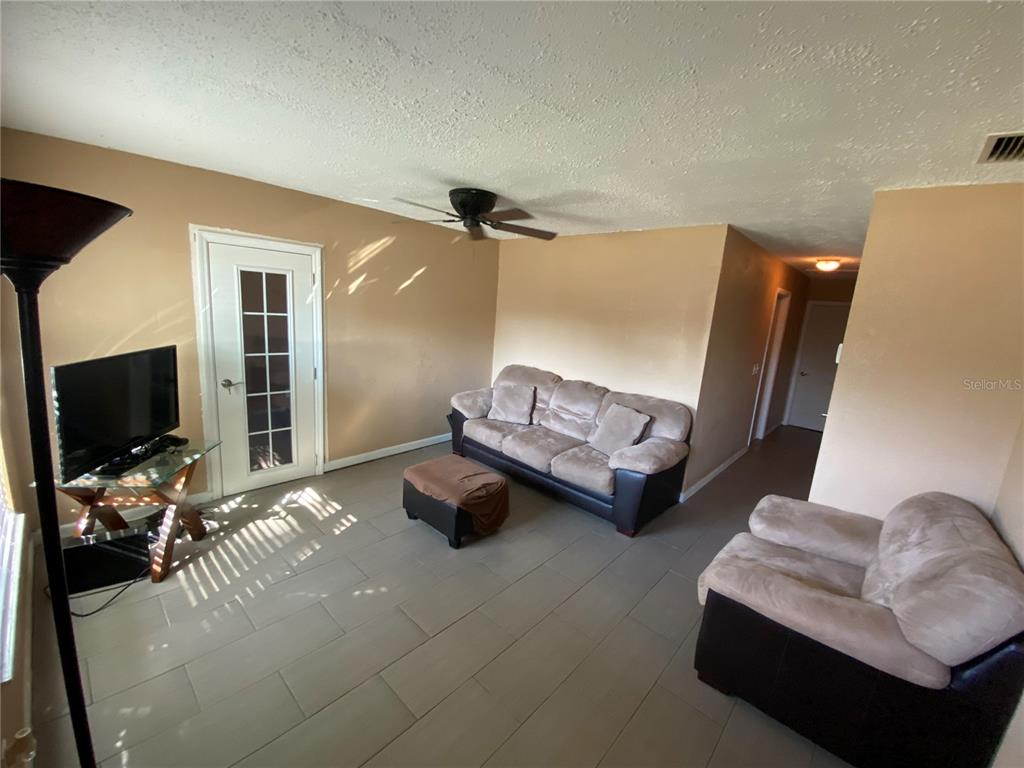 A living room features light-colored walls, gray tile flooring, a sofa, and a ceiling fan — 4403 GANDY CIRCLE, TAMPA, FL