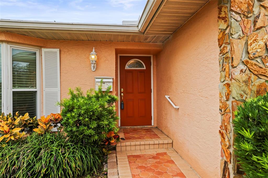 A front entrance with a red door, stone siding, and a tiled walkway — 1112 40TH AVE NE, ST PETERSBURG, FL