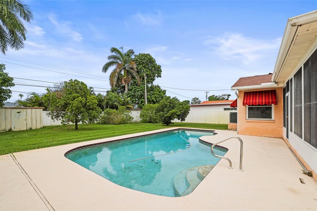 A backyard features a swimming pool, a concrete patio, and a grassy lawn with trees — 1112 40TH AVE NE, ST PETERSBURG, FL