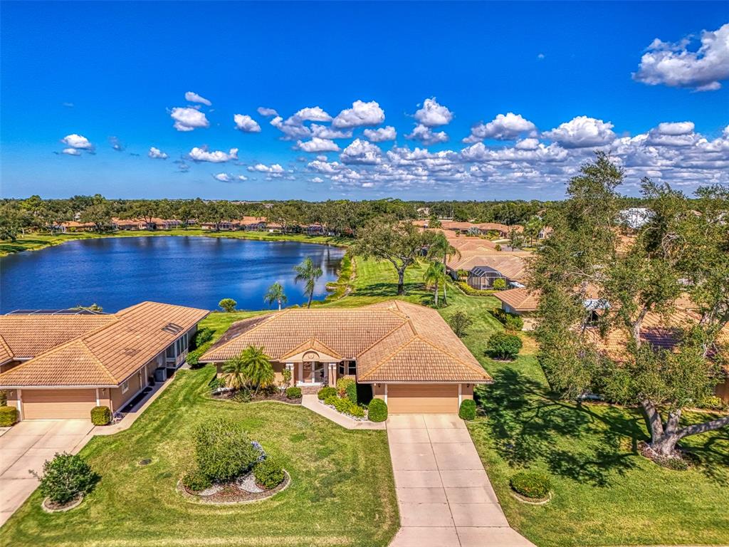 An aerial view shows a single-story house with a tile roof and a lake nearby — 3168 E VILLAGE DRIVE, VENICE, FL