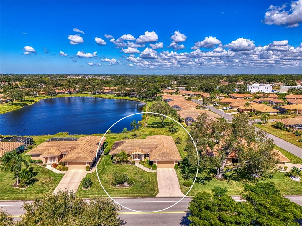 An aerial view shows a single-story house with a tan roof and driveway near a lake — 3168 E VILLAGE DRIVE, VENICE, FL