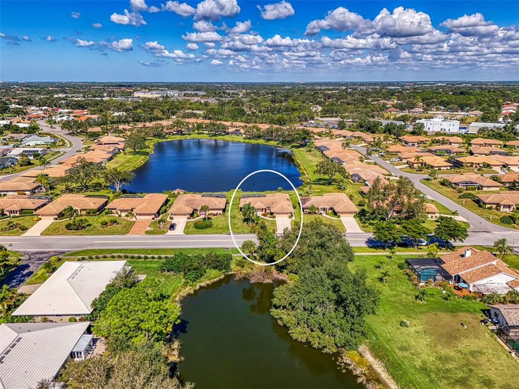 An aerial view shows a residential neighborhood with houses surrounding a lake — 3168 E VILLAGE DRIVE, VENICE, FL