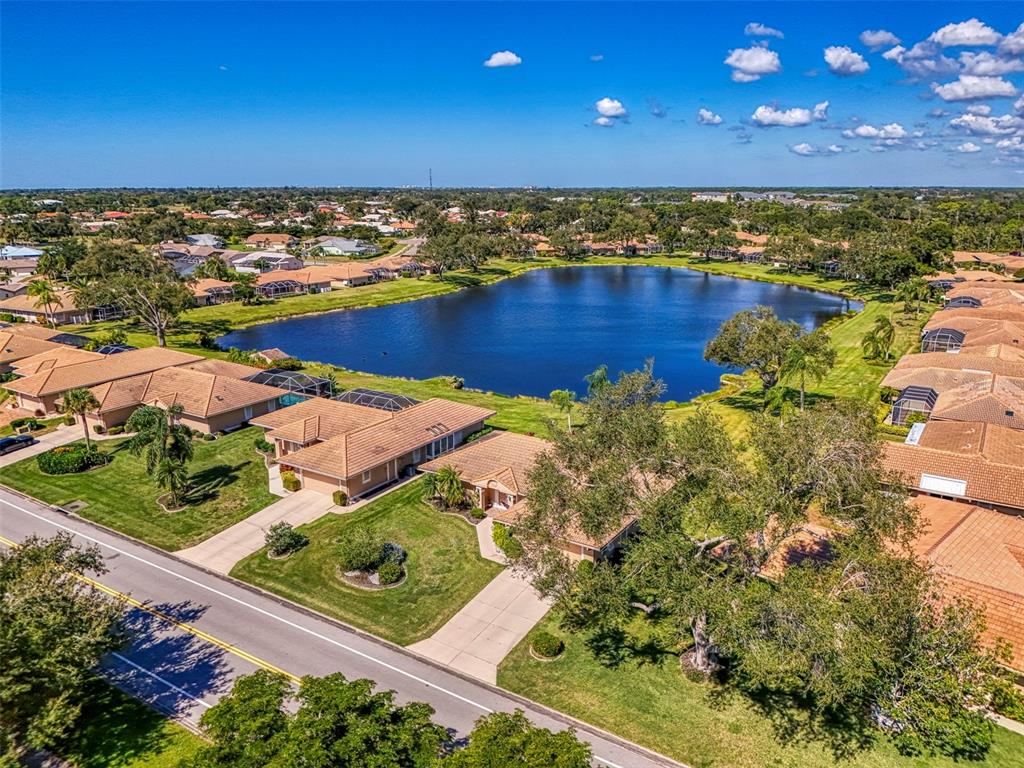 An aerial view of a suburban neighborhood featuring houses surrounding a large, central lake — 3168 E VILLAGE DRIVE, VENICE, FL