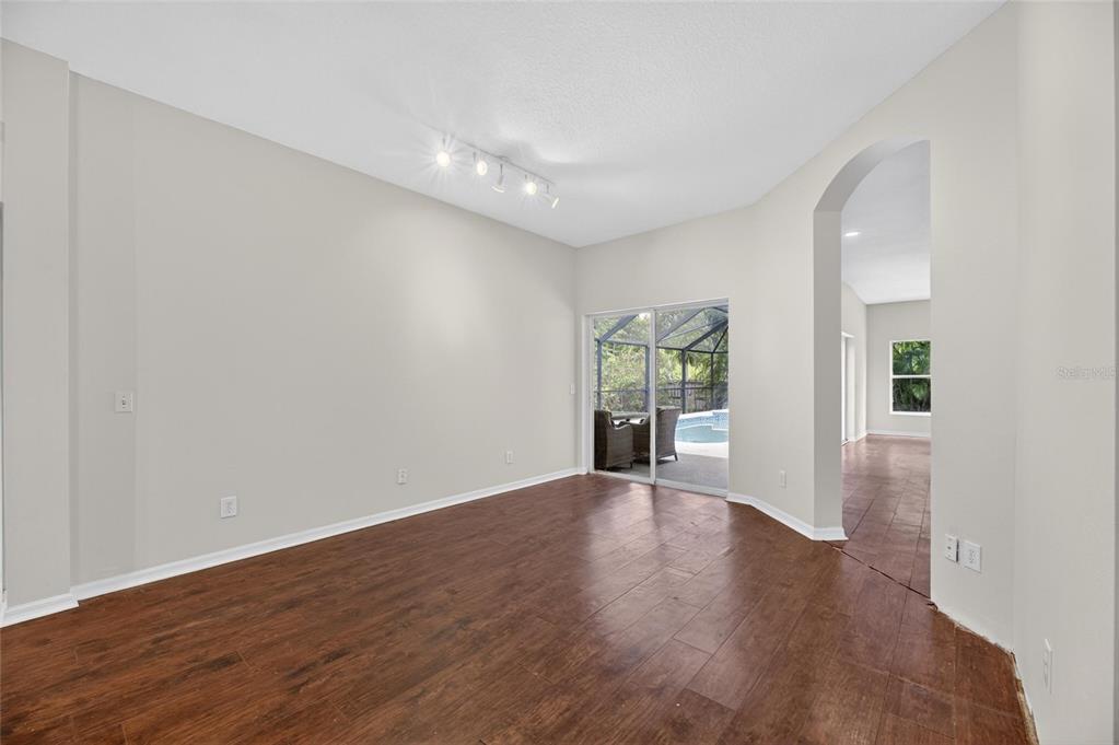 An empty room with dark wood-look flooring, light walls, and a sliding door to a pool — 11901 NORTHUMBERLAND DRIVE, TAMPA, FL