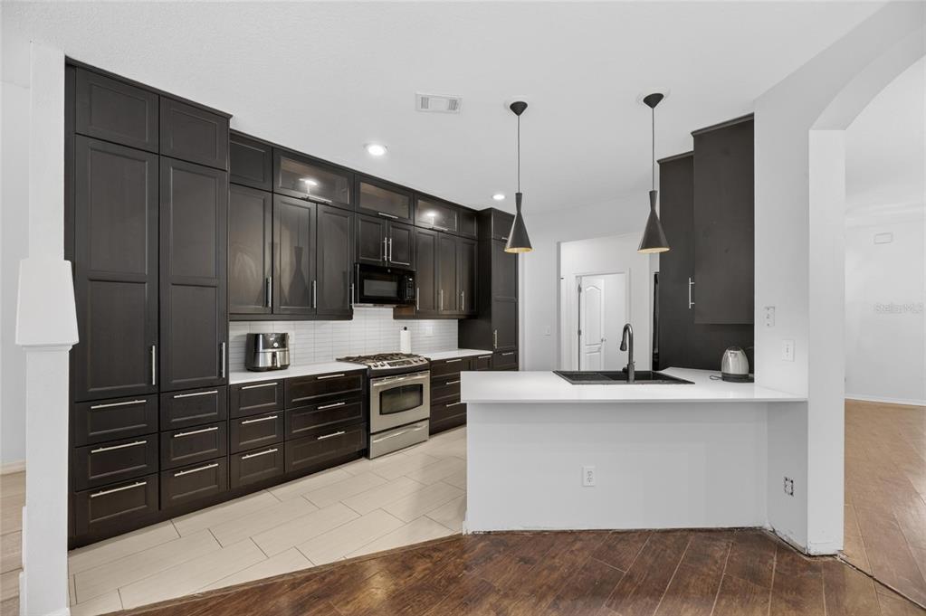 A kitchen features dark wood cabinetry, white countertops, stainless steel appliances, and two pendant lights — 11901 NORTHUMBERLAND DRIVE, TAMPA, FL