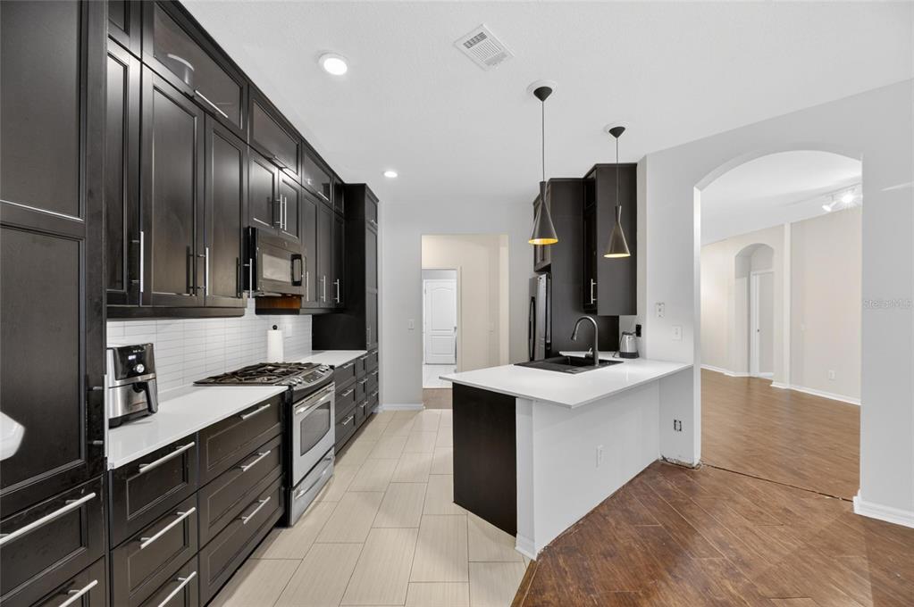 A modern kitchen features dark wood cabinets, white countertops, stainless steel appliances, and tile flooring — 11901 NORTHUMBERLAND DRIVE, TAMPA, FL