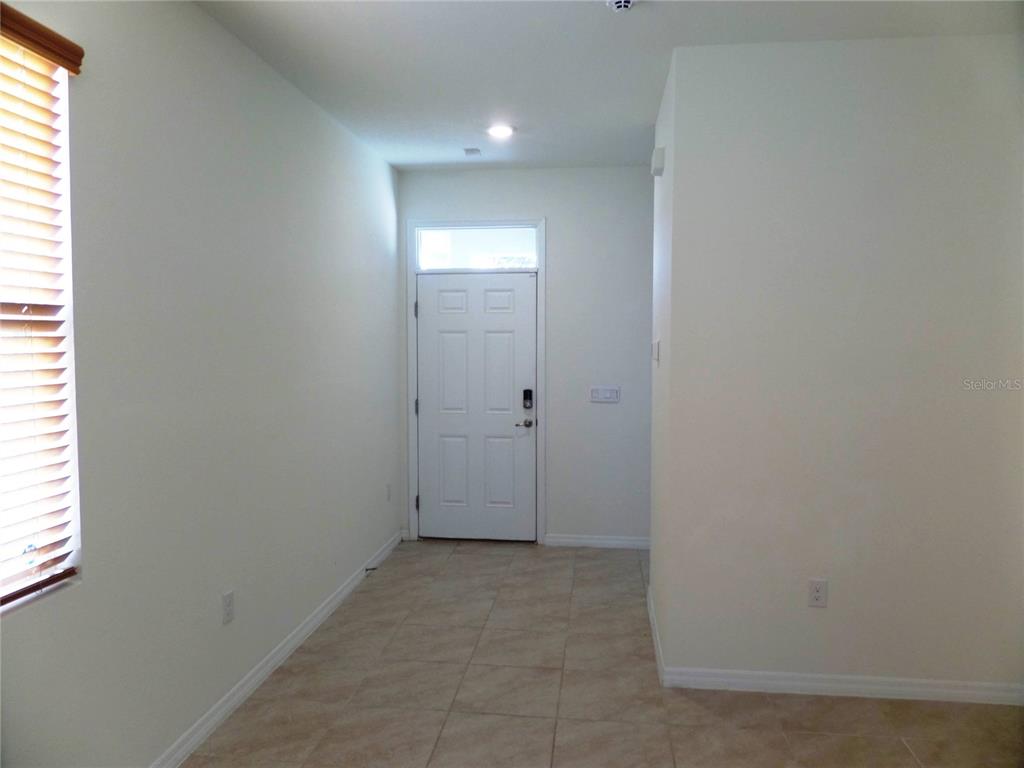 An entryway features a white front door, light-colored tile flooring, and a window with blinds — 8051 PENROSE PLACE, WILDWOOD, FL