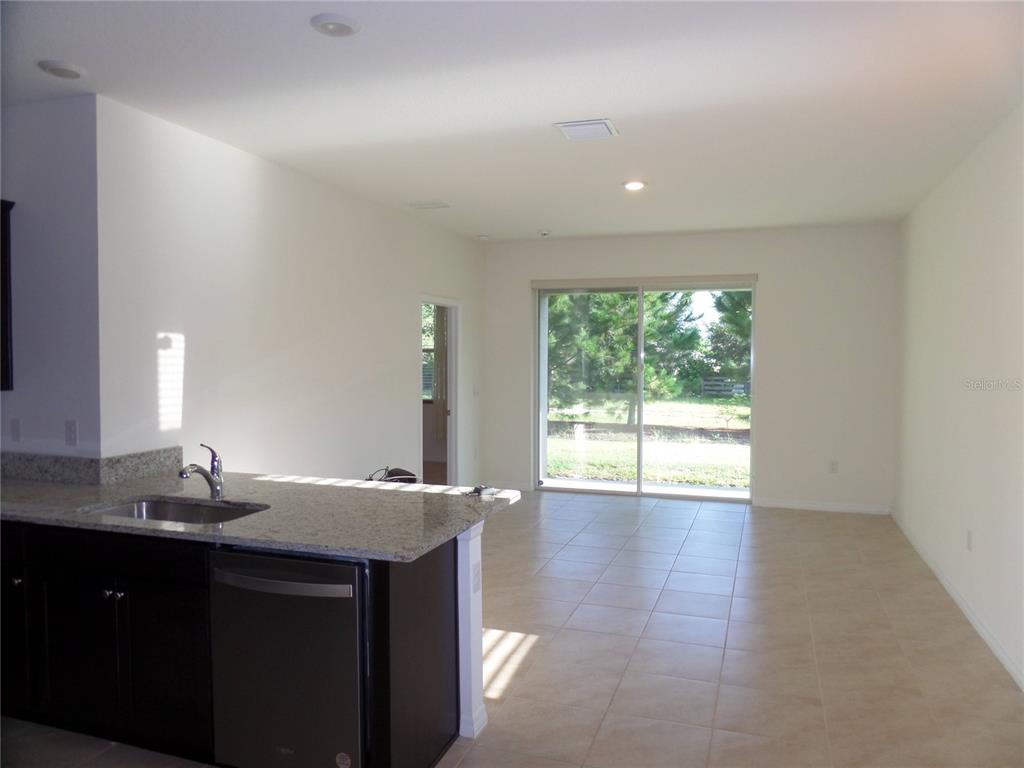 A kitchen with dark cabinets and granite countertops overlooks an open living area with tile — 8051 PENROSE PLACE, WILDWOOD, FL