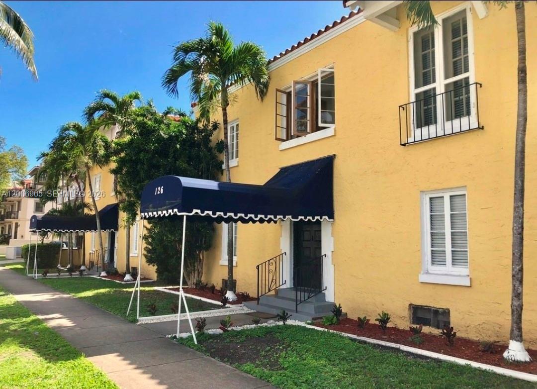 A yellow two-story building features a blue awning over the entrance and white-trimmed windows — CORAL GABLES, FL