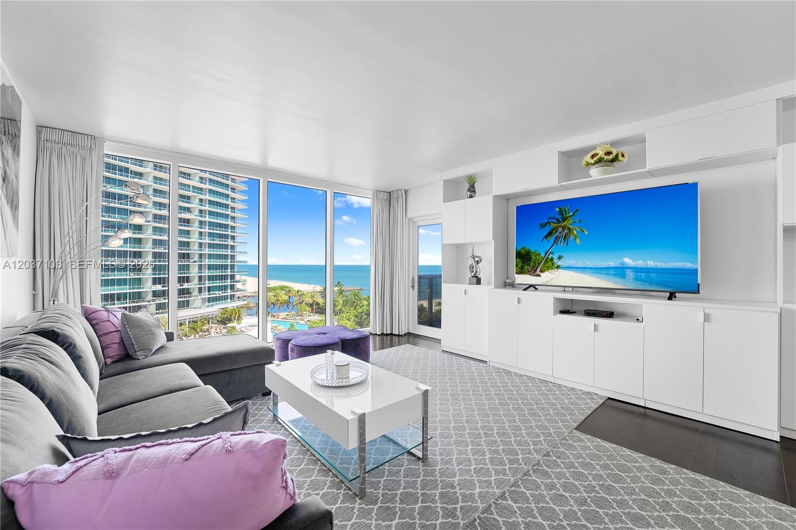 A living room features a grey sectional sofa, white media console, and floor-to-ceiling ocean views — 10275 Collins Ave # 807, Bal Harbour FL 33154, BAL HARBOUR, FL