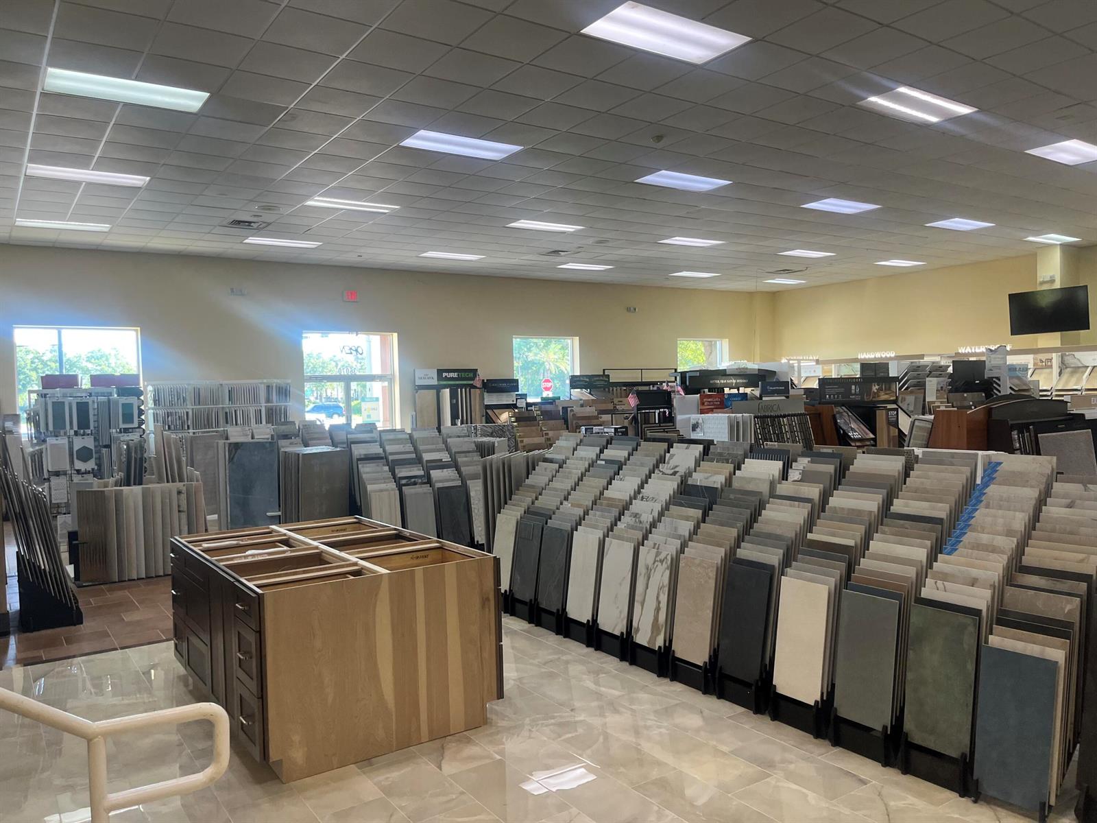 A showroom displays numerous tile and flooring samples arranged on racks with a central cabinet — 36070 Emerald Coast Parkway, FL 32541, FL